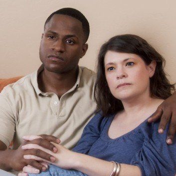 Photo of a interracial couple holding hands, looking serious.