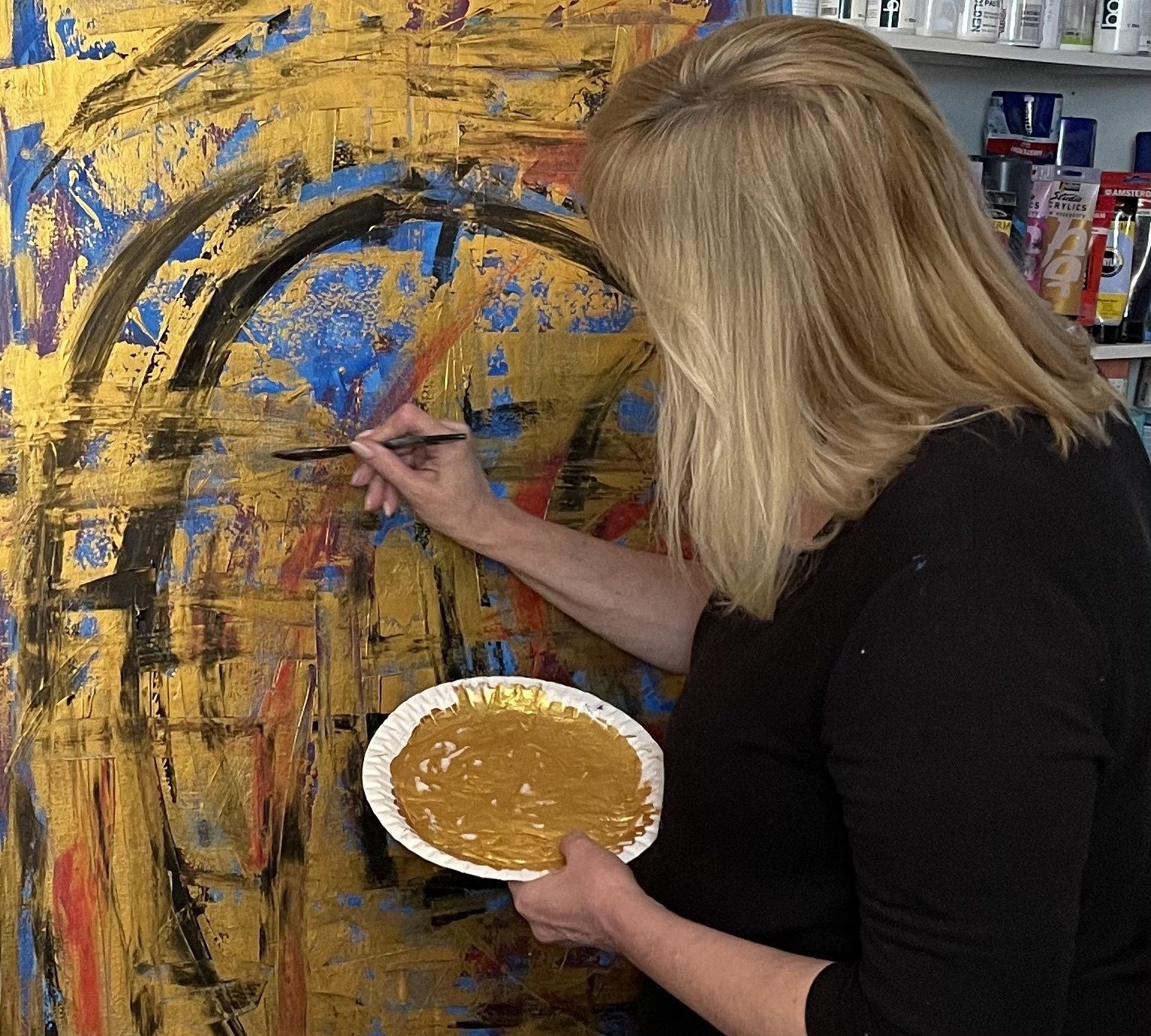 Simone Braun holding a brush and a palette in front of her artwork painting