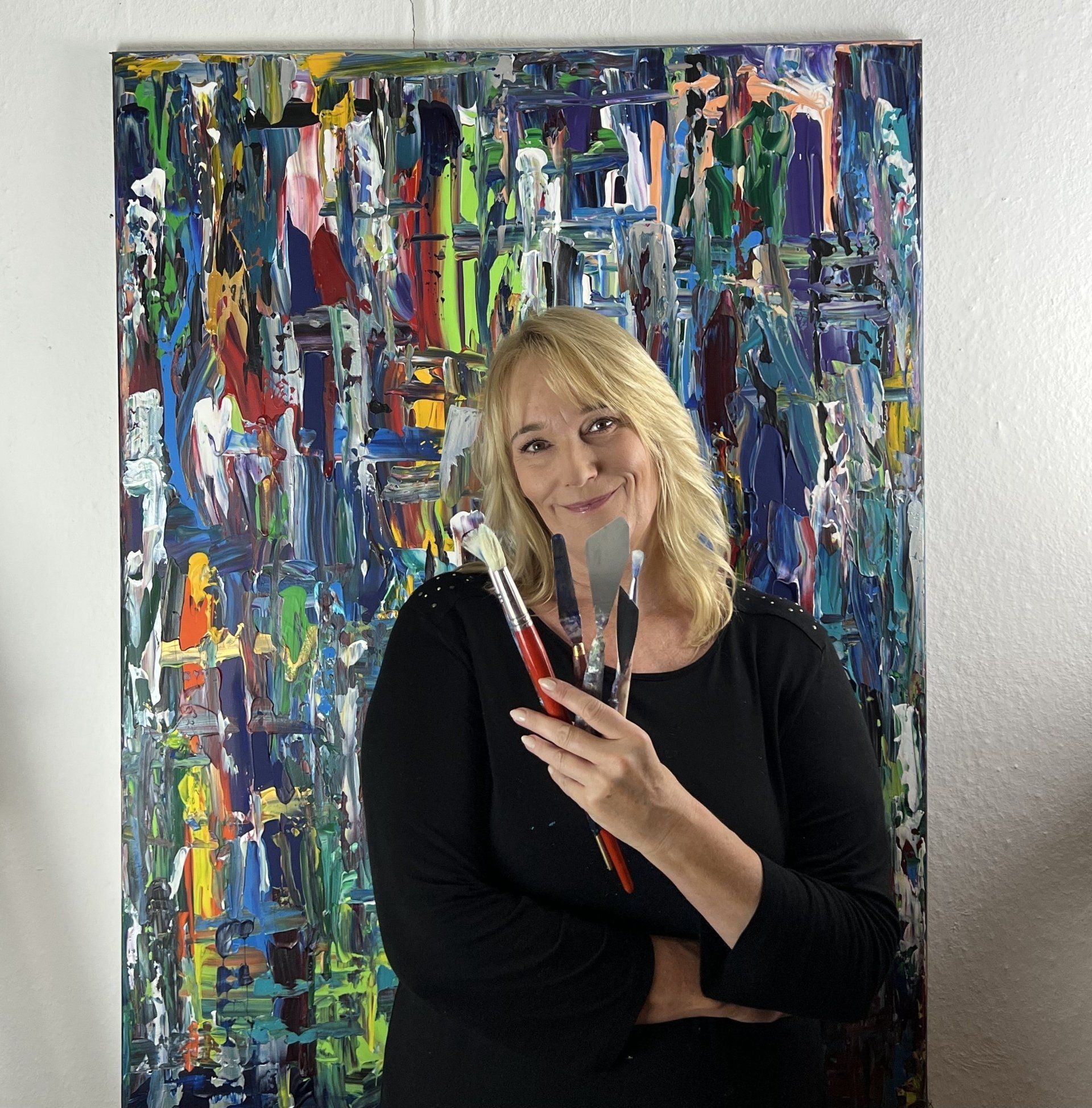 Künstlerin Simone Braun mit Pinseln in den Händen vor einem ihrer Kunstwerke