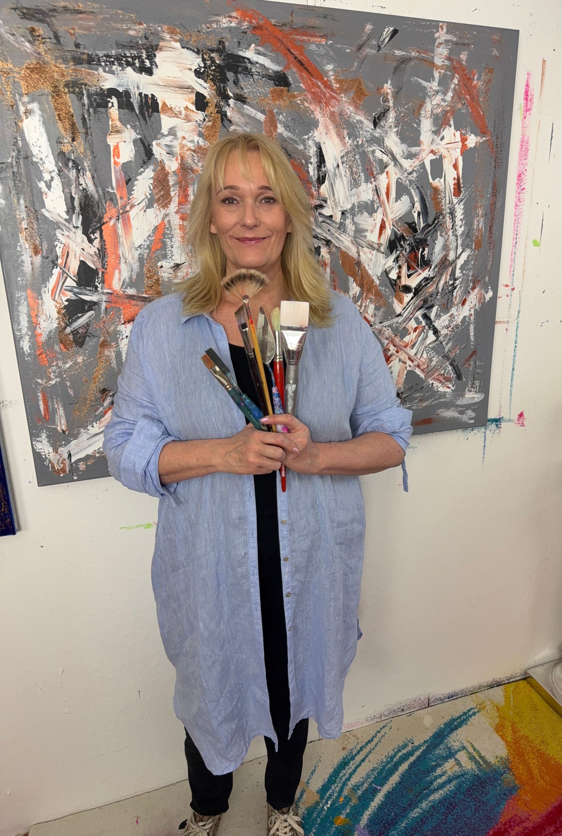 Simone Braun mit Pinseln in den Händen vor einem ihrer Kunstwerke