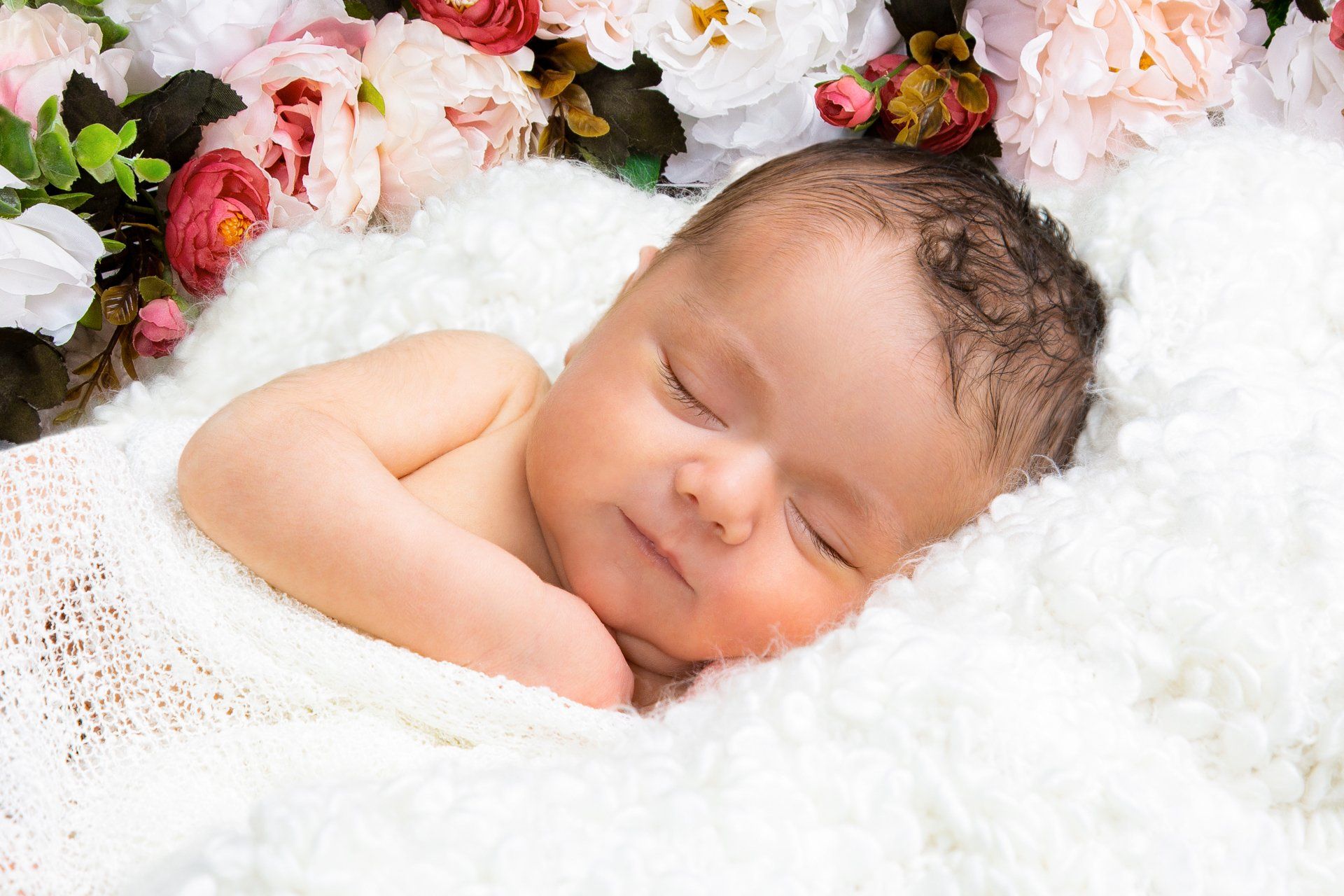 Baby auf weißer Decke mit Blumenkranz