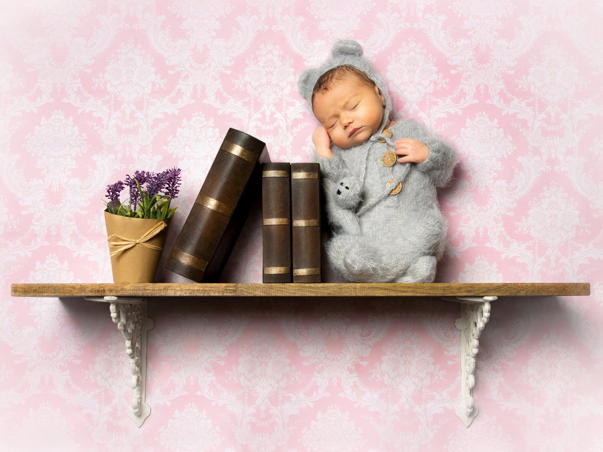 Newborn mit Teddymütze auf Bücherregal