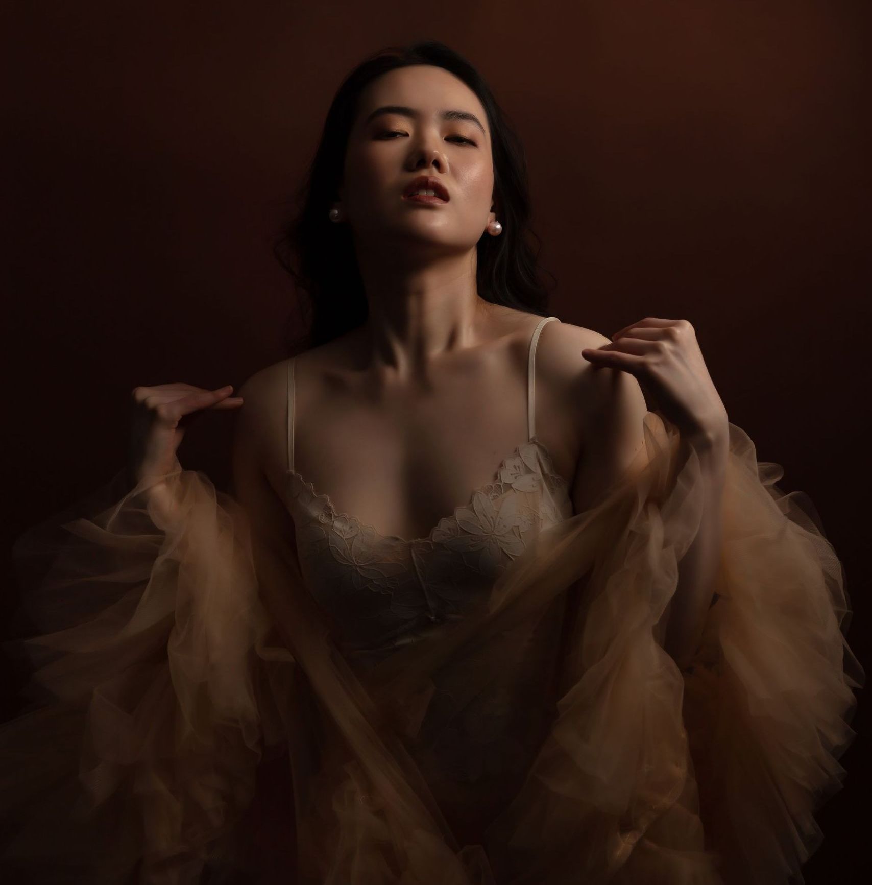 An Asian woman in her 20s is wrapped in a tulle robe and floral lingerie. The colours are ethereal, and the tone is moody and sensual.