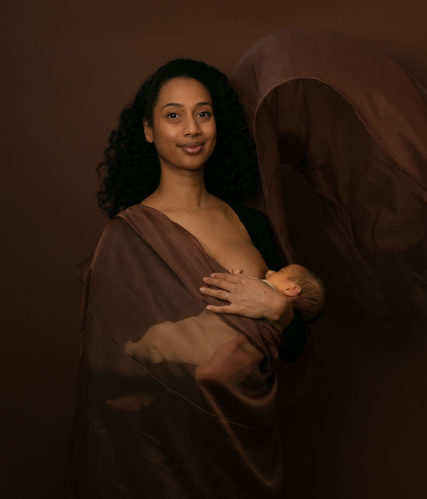 A woman in a glamorous portrait breastfeeding her newborn baby.