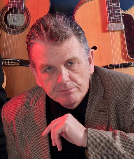 musician head and shoulders serious looking in front of guitars