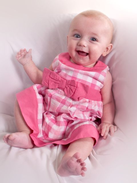 happy baby girl baby in pink dress full length sitting and smiling