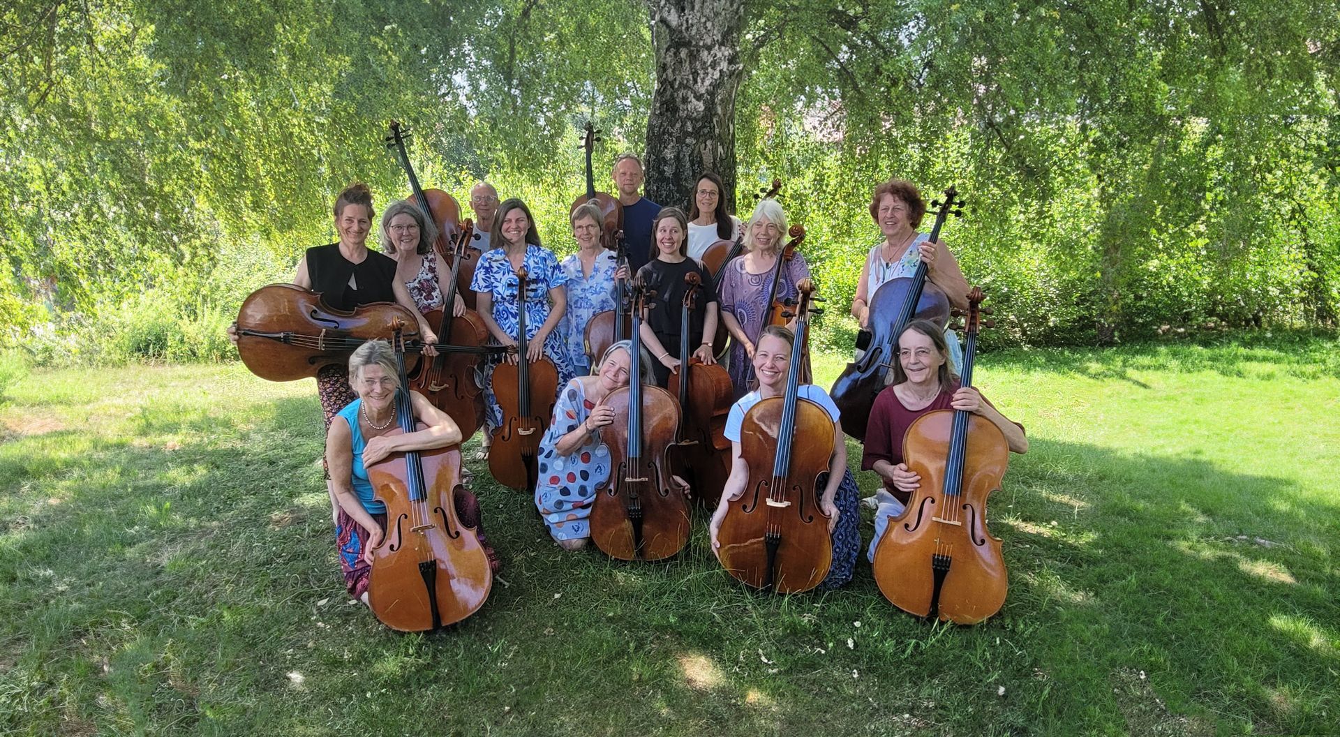 Sue Schlotte mit einer Gruppe von Workshopteilnehmer*innen, alle mit ihrem Cello in der Hand, vor einem Baum.