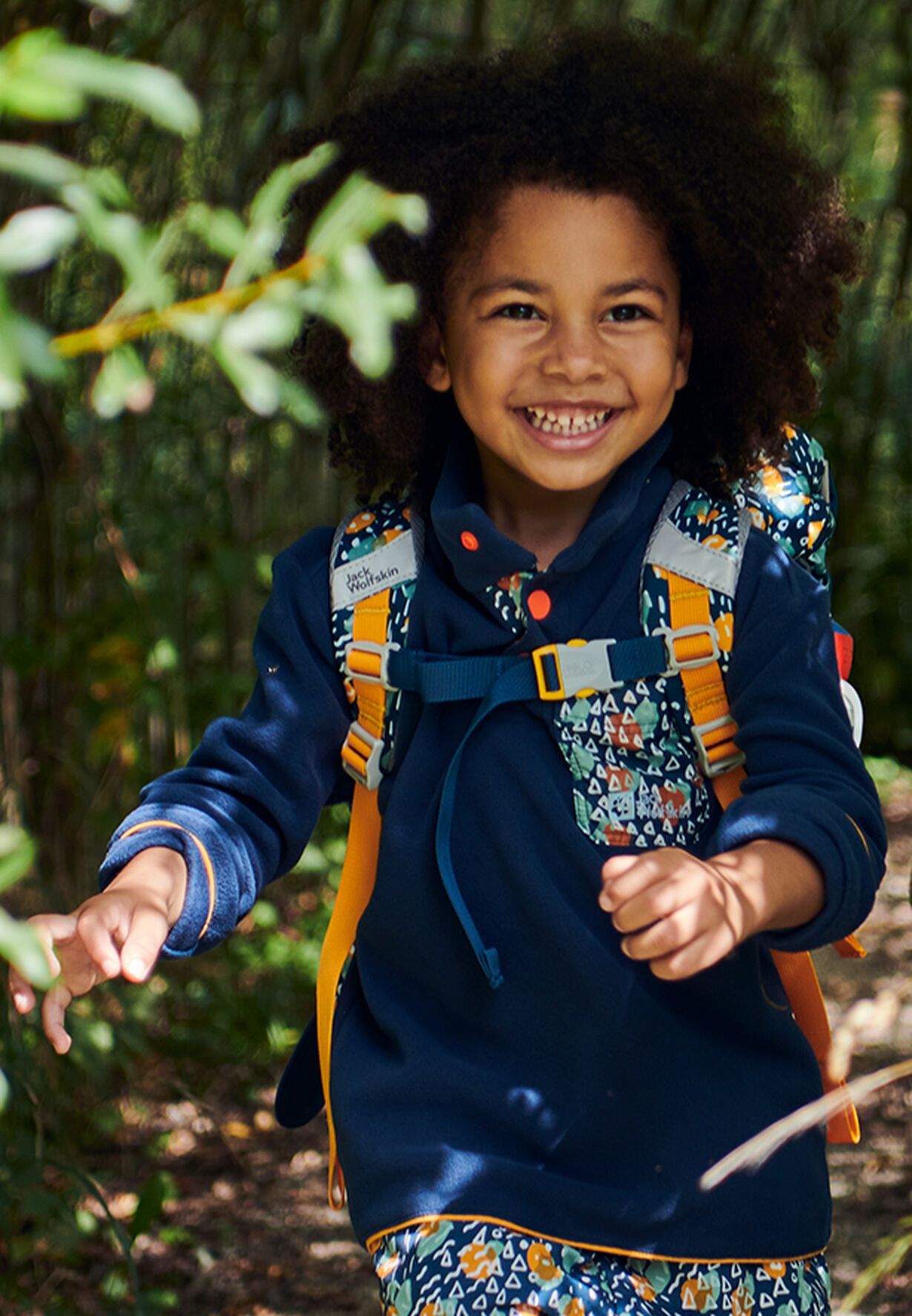 Junge mit Rucksack bei einem Outdoor-Shooting im Grünen – gestylt für eine sportliche Kinderkampagne einer Modemarke.