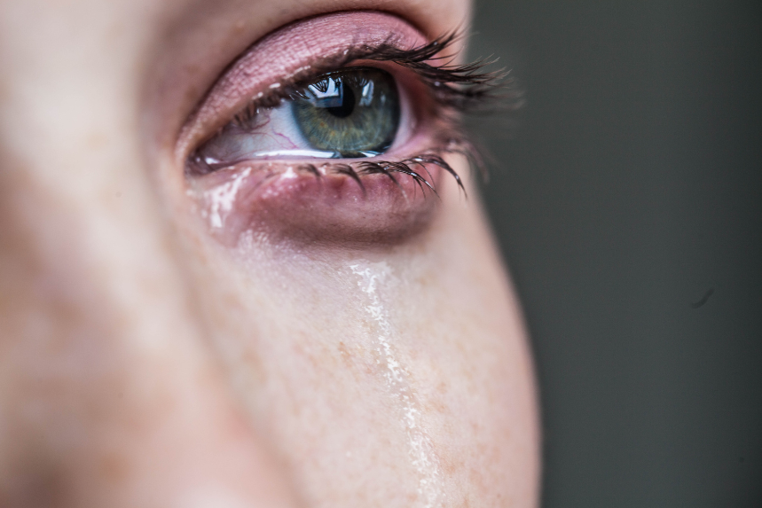 ein gerötetes, tränendes Auge. Eine Träne läuft über die Wange