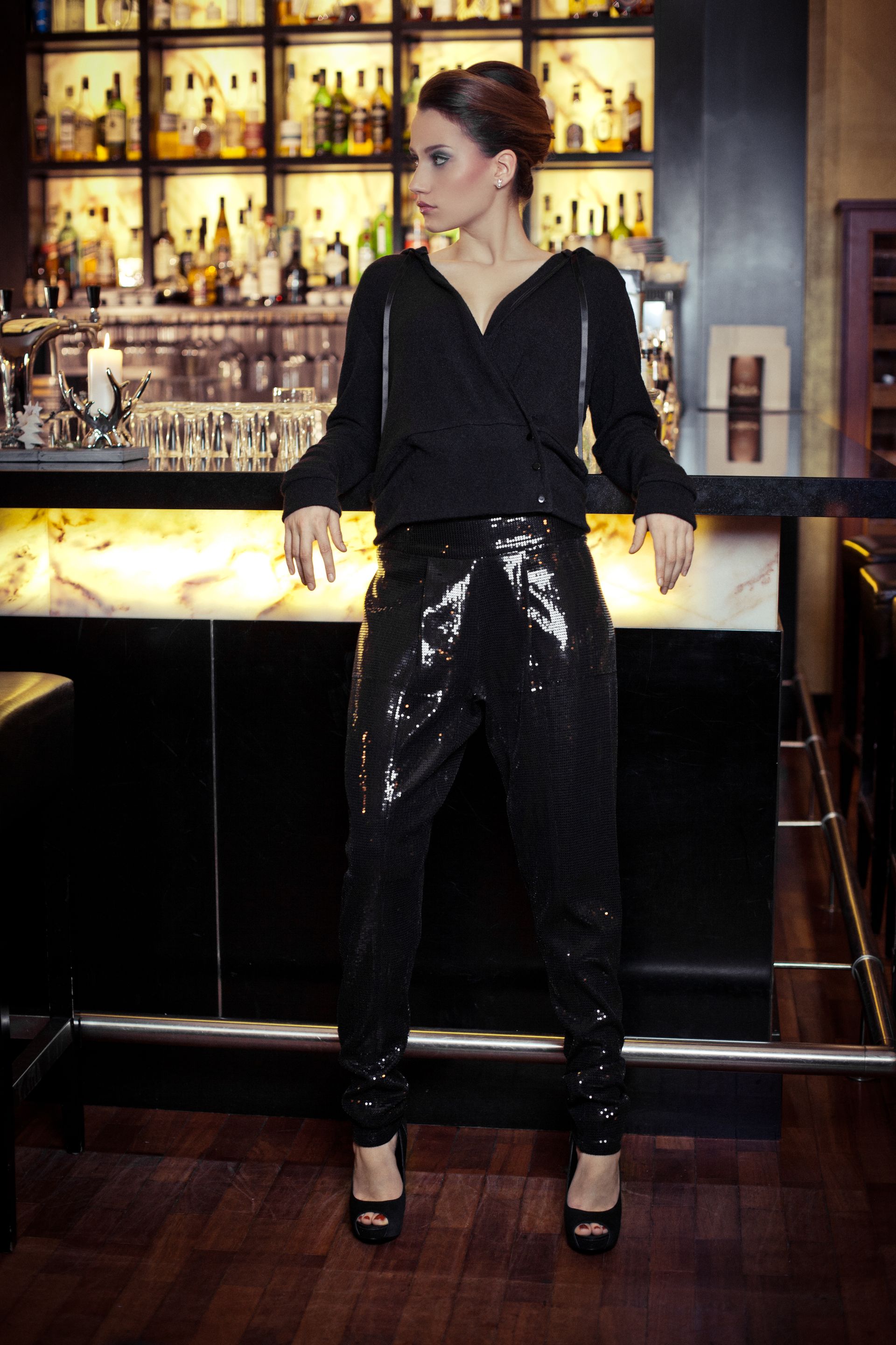 Frau lehnt an einer Bar und ist in schwarz gekleidet. Marke der Kleidung ist 3 Zehn.