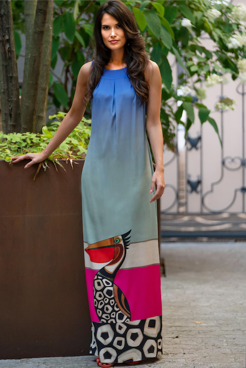 Frau mit langen, lockigen, braunen Haaren steht vor einer Pflanze und trägt ein buntes, bodenlanges Sommerkleid der Marke Rhoda K. Make-up ist ausdrucksstark in natürlichen Tönen.