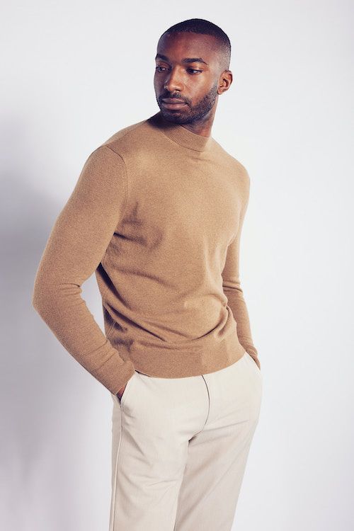 Männermodel mit beigefarbenem Pullover und weißer Hose.
