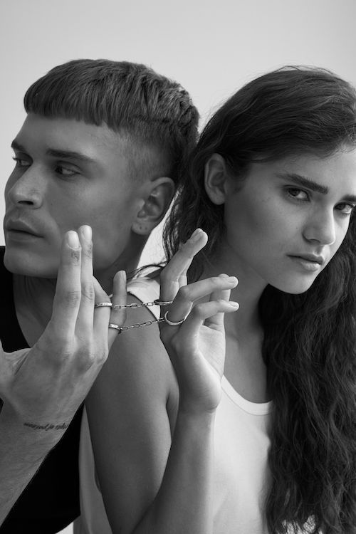 Schwarz/weiß Bild zeigt eine junge Frau mit dunklen, naturgelockten Haaren und einen jungen Mann mit modernem Kurzhaarschnitt. Beide tragen Schmuck der Marke purman.