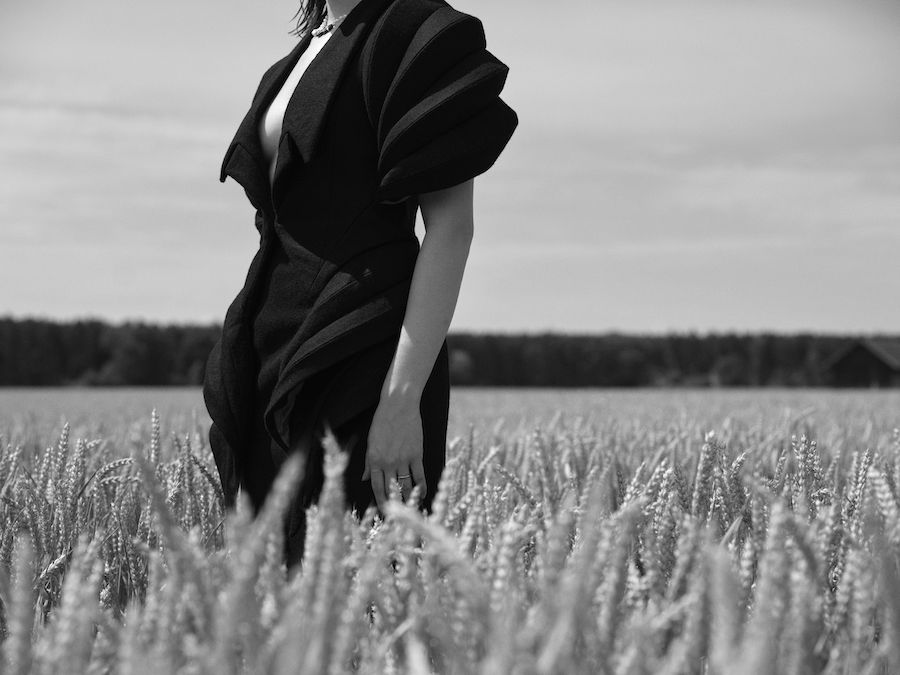 Schwarz Weiß Foto. Eine Dame in einem schwarzen Kleid steht im Kornfeld, man sieht nur den Körper