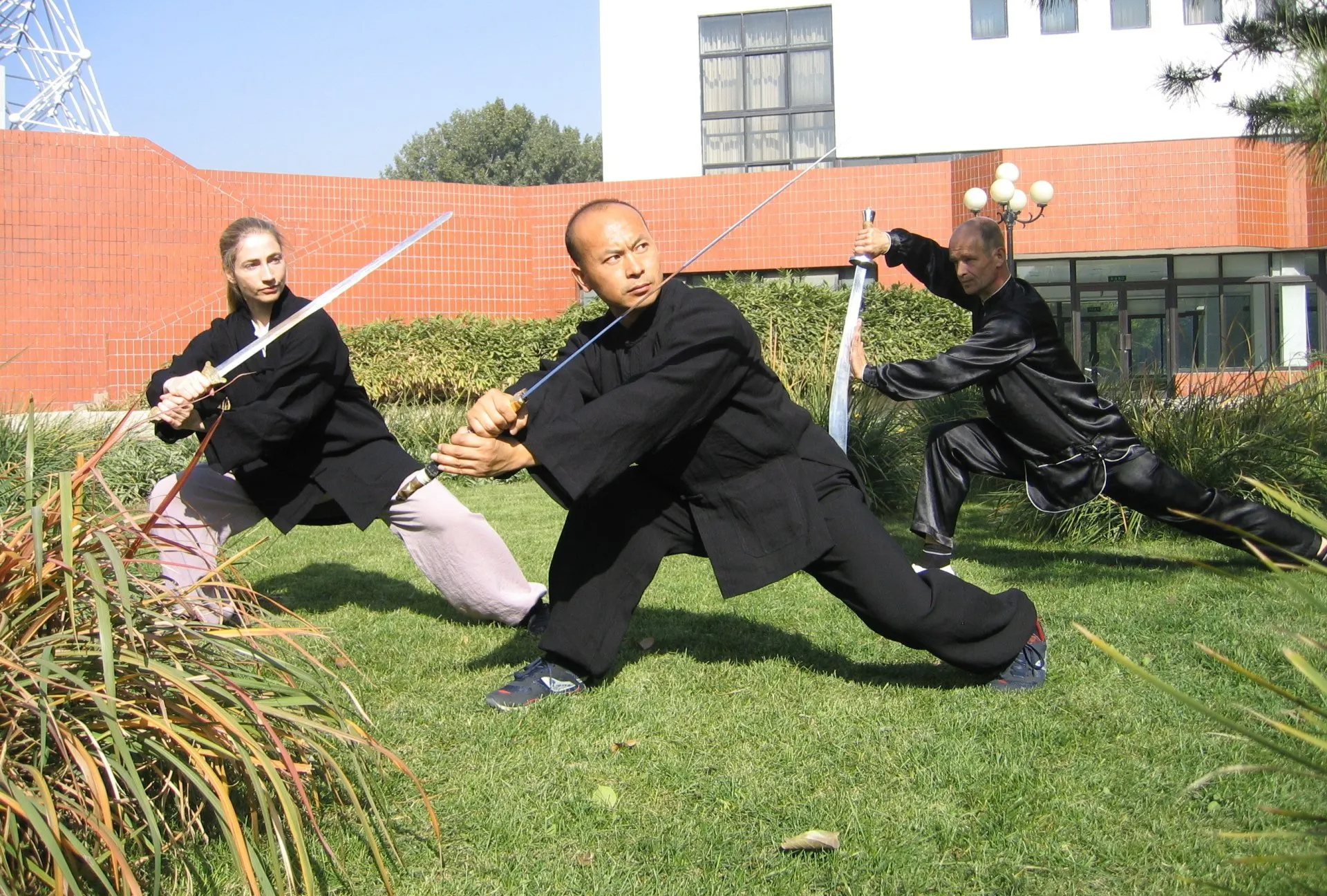 Drei Personen trainieren mit Schwertern auf dem Campusgelände in Beijing