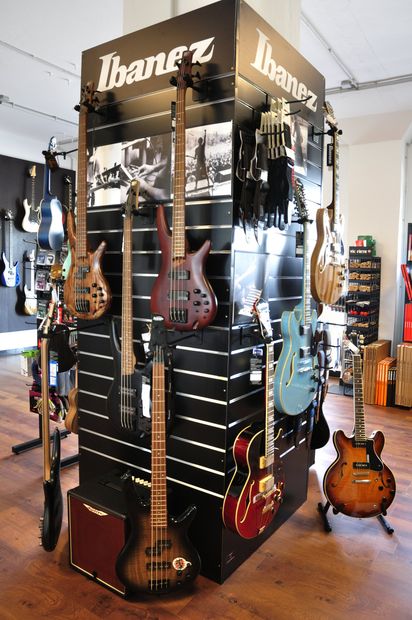 Ein Pfeiler im Verkaufsraum an dem E-Gitarren und E-Bässe präsentiert sind.