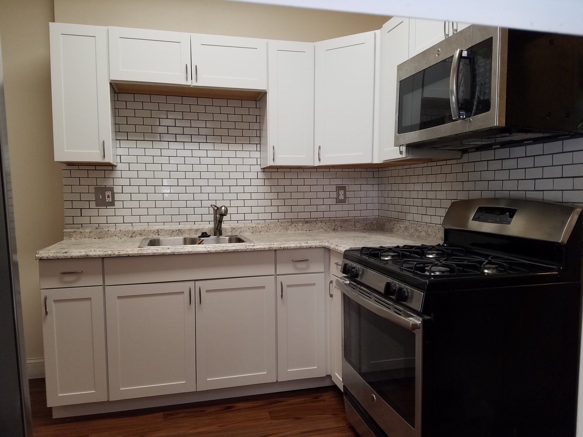 Full kitchen remodel in Philadelphia row home with large granite countertops, white subway tile backslash, white upper and lower cabinets and black appliances