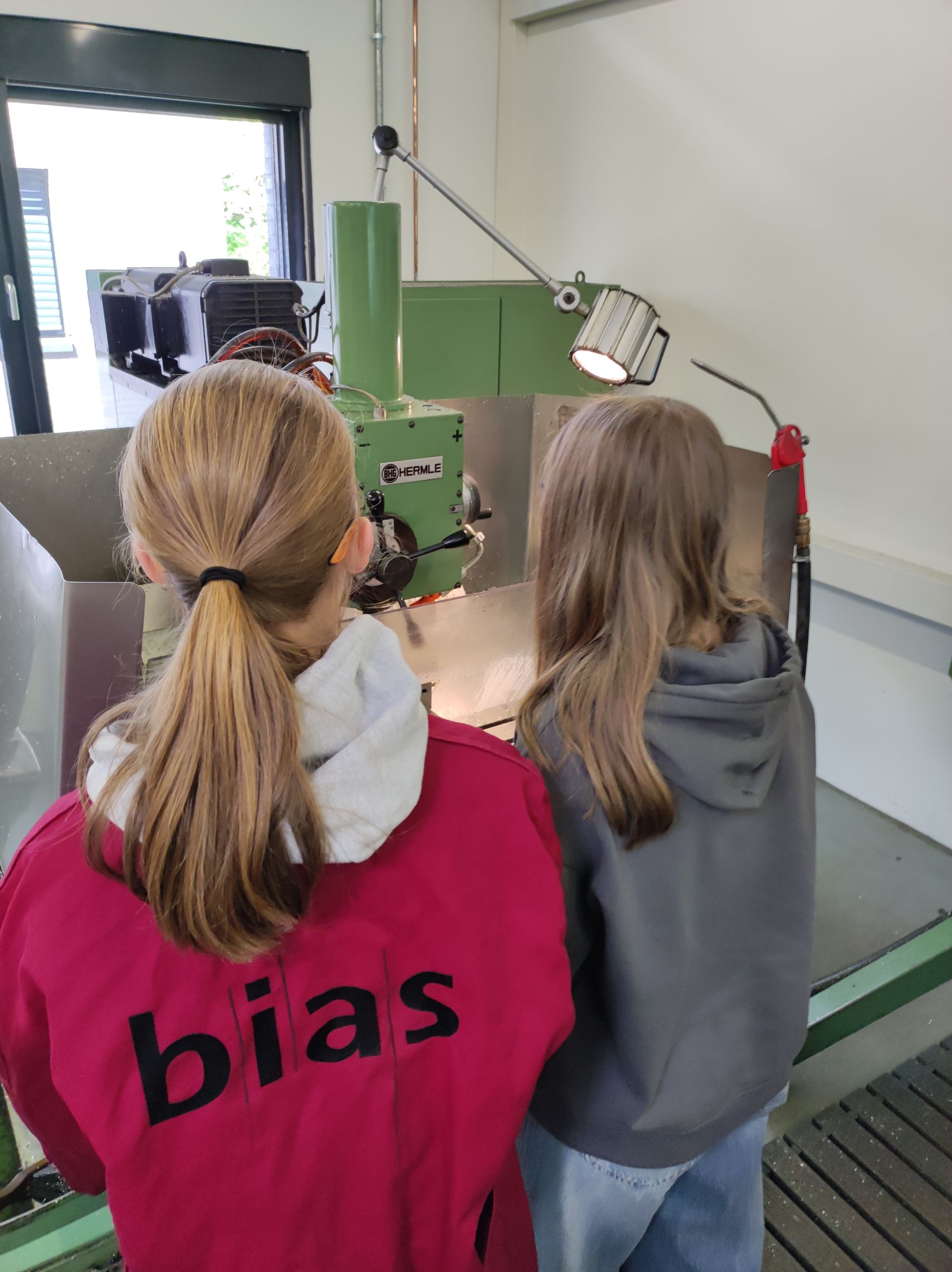 Mädchen stehen in einer Werkstatt, ein Trägt einen Kittel mit der Aufschrift BIAS