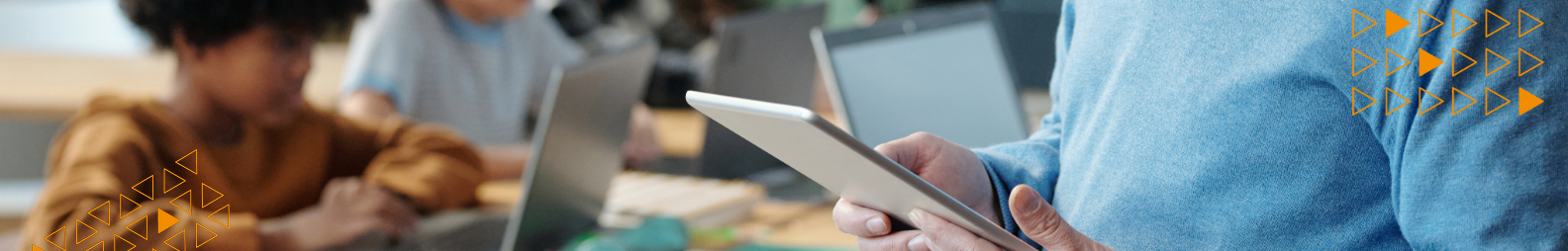 Schüler arbeiten an Notebooks; der Lehrer hat ein Tablet in der Hand