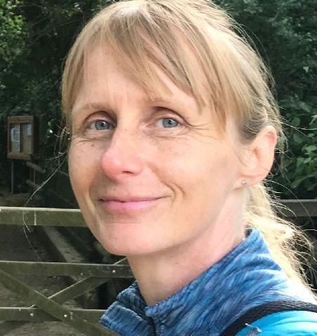 Head and shoulders shot of white woman with long blonde hair. Background is a park.