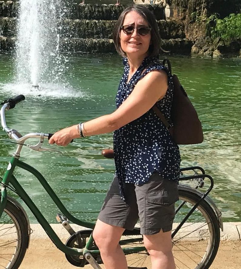 Sunny day image of a woman (Sally) holding a Dutch-style bike in front of a water feature