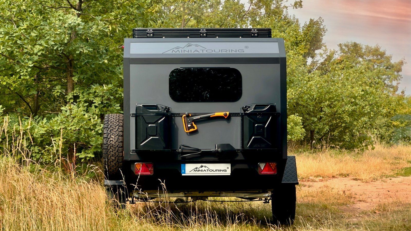 Heckansicht des MINIATOURING M23 Offroad-Wohnwagens mit Kanistern und Axt