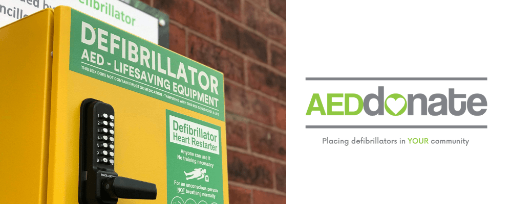 A yellow defibrillator locker placed on a brick wall. On the right hand side of the image is the AEDdonate logo in green and grey (tagline: placing defibrillators in your community)