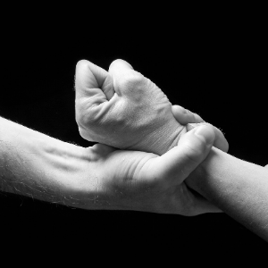 Mano sujetando con fuerza un brazo con puño cerrado
