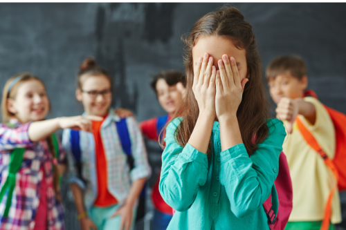 bullying Niña tapándose la cara con las manos mientras sus compañeros se ríen de ella y la señalan por detrás