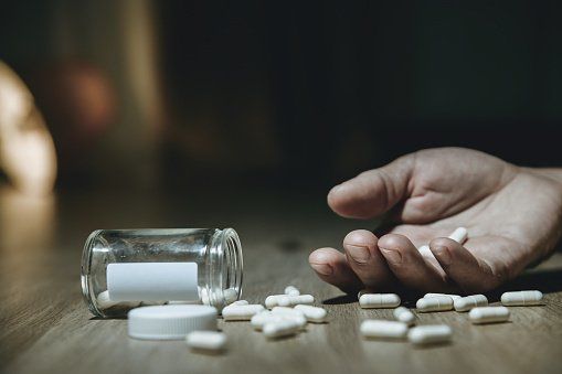 Drogodependencia Mano en el suelo con pastillas al lado de un bote de pastillas derramado