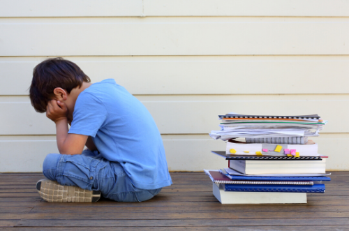 Dificultades aprendizaje Niño sentado en el suelo cubriéndose la cara disgustado con una pila de libros a su lado