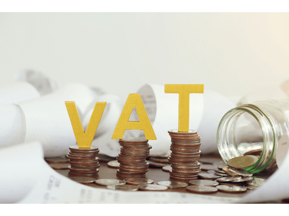 Letters VAT onto of a stack of coins and paperwork surrounding