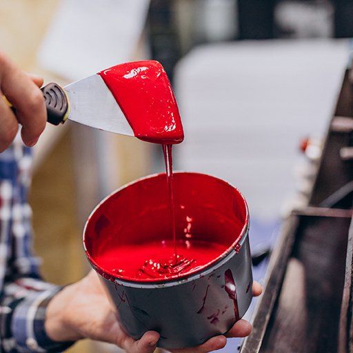 Farbe Ein Mitarbeiter trägt rote Farbe aus einem Farbeimer auf eine Spachtel.
