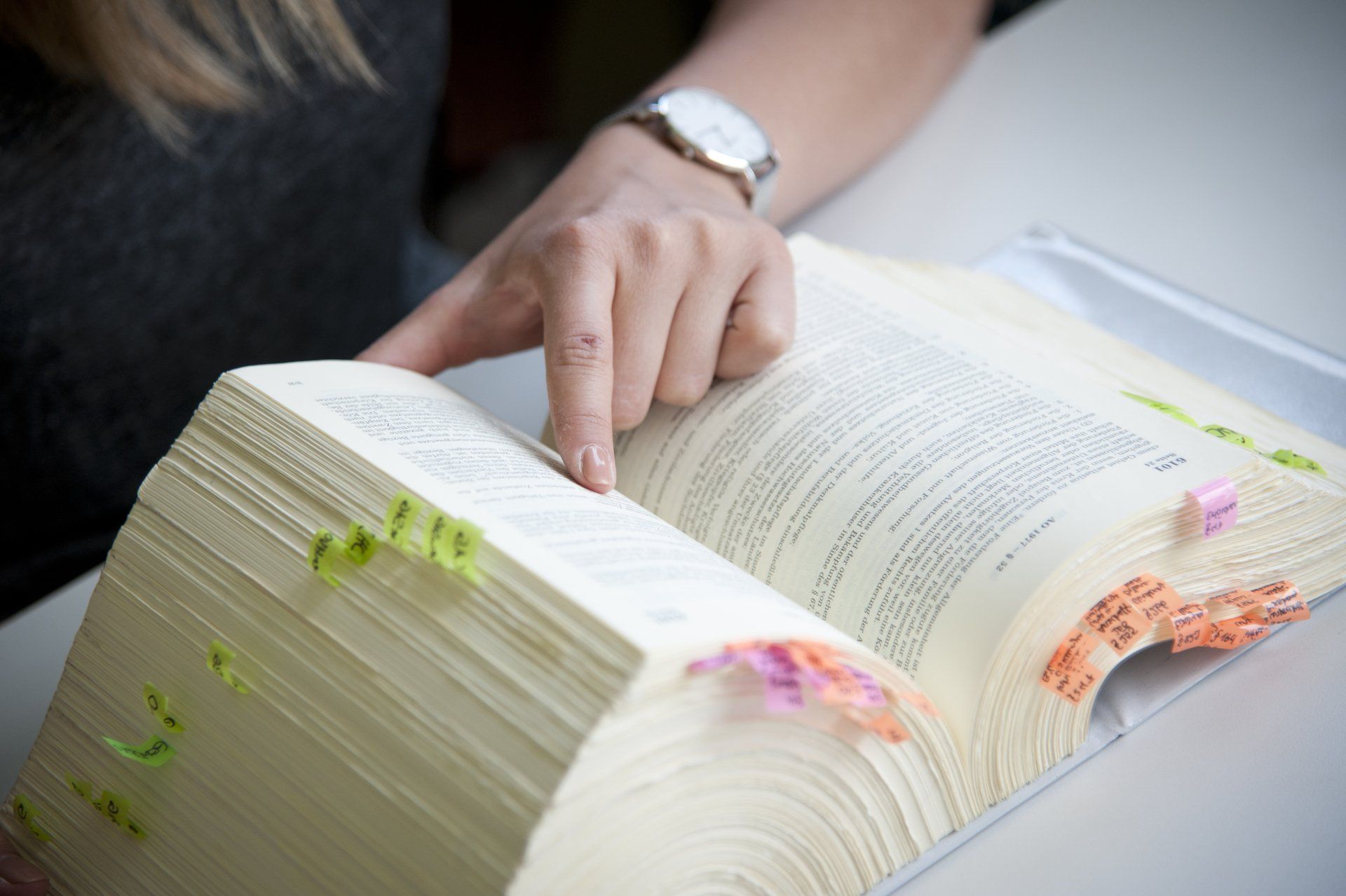 Person mit Uhr am Handgelenk liest mit dem Finger in einem Gesetzbuch mit Markierungen