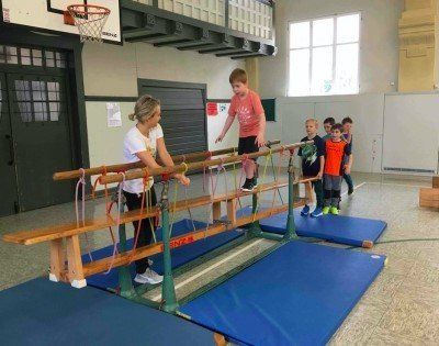 Kinder machen sportliche Übungen an einem Barren in der Turnhalle