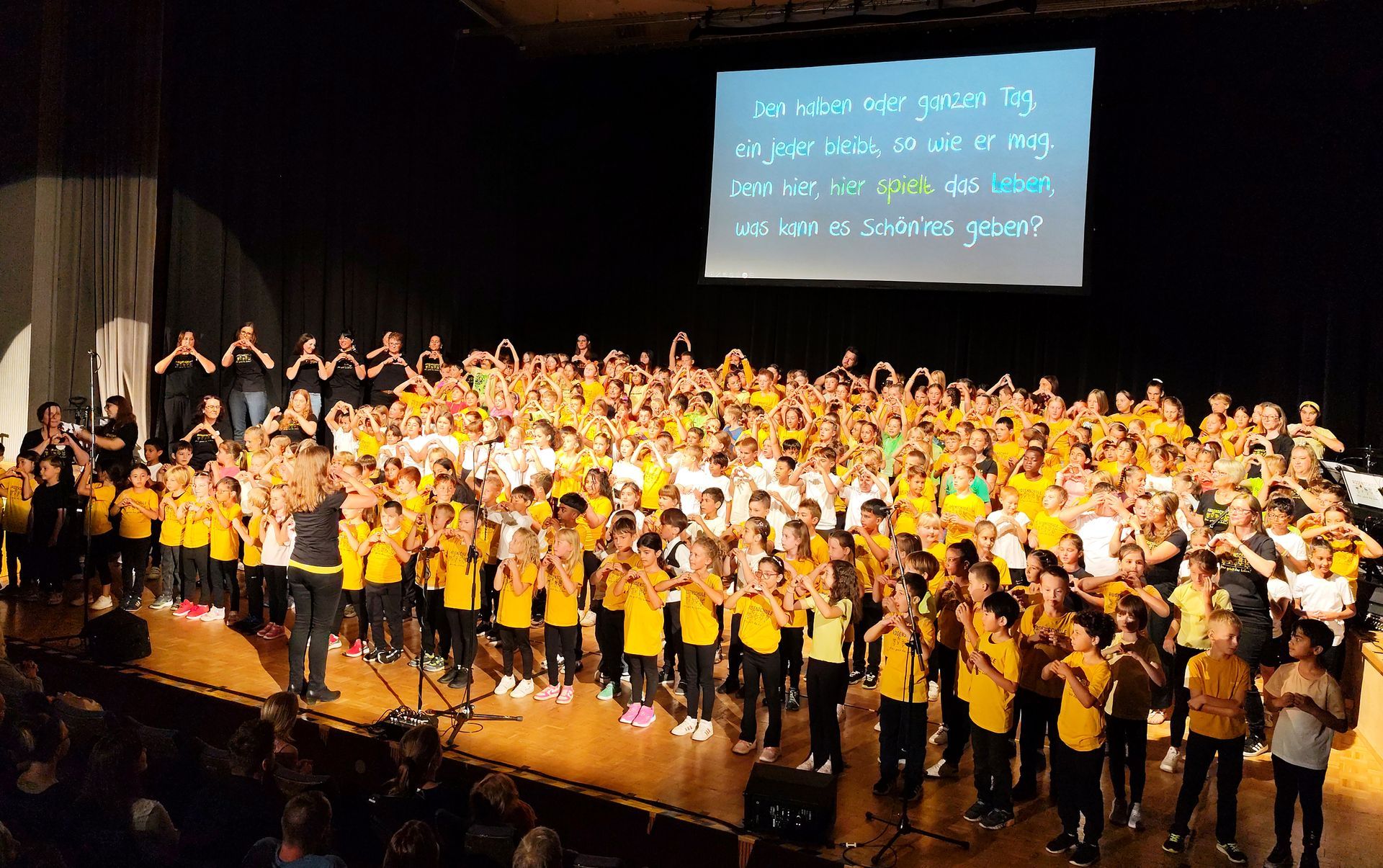 Präsentation des Rosenschulsongs Finale der Jubiläumsfeier auf der Bühne des Konzerthauses:
Das kompette Team aus Kindern, Lehrerinnen, Lehrern, pädagogischen Assistentinnen und Betreuungskräften performt im Schul-Tshirt den Rosenschulsong.