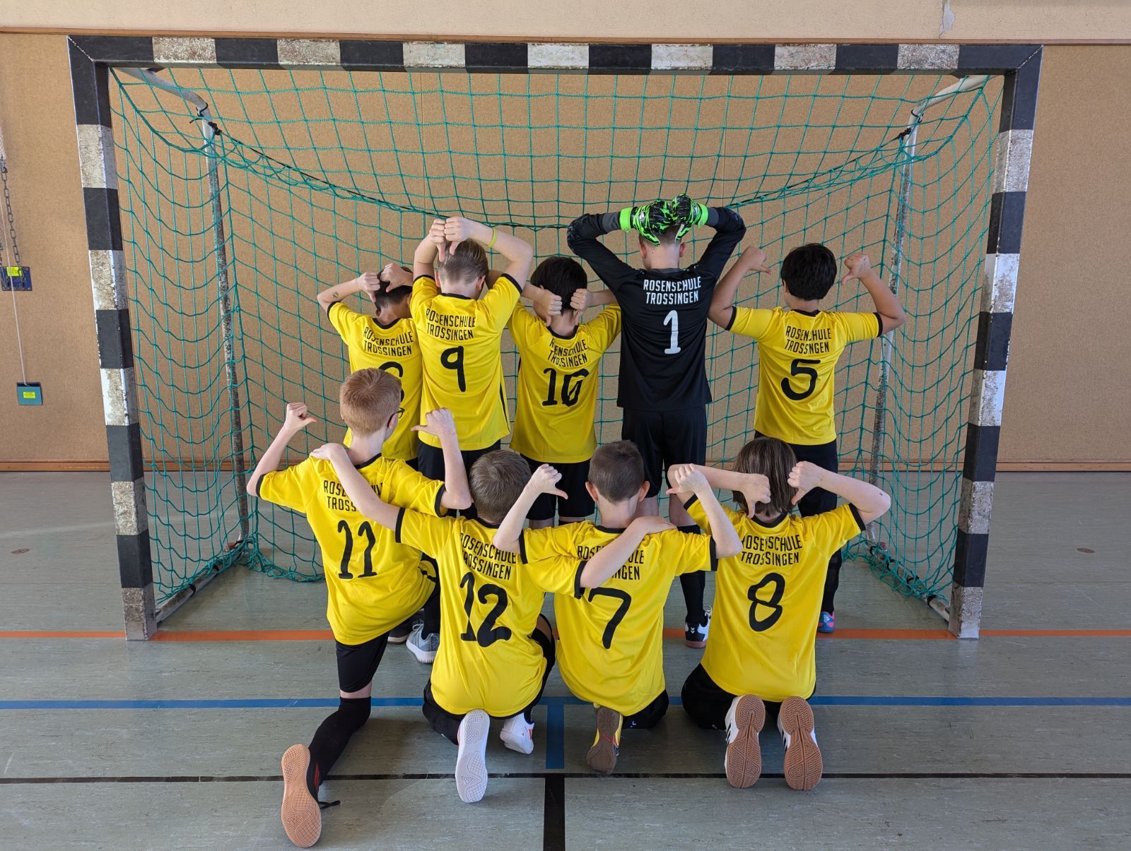 Mannschaftsfoto Rückansicht Mannschaftsbild Fußballmannschaft der Rosenschule. 9 Schüler der Schulmannschaft stehen in schwarz-gelben Fußballtrikots in einem Hallenfußballtor und zeigen die Rückansicht der neuen Trikots