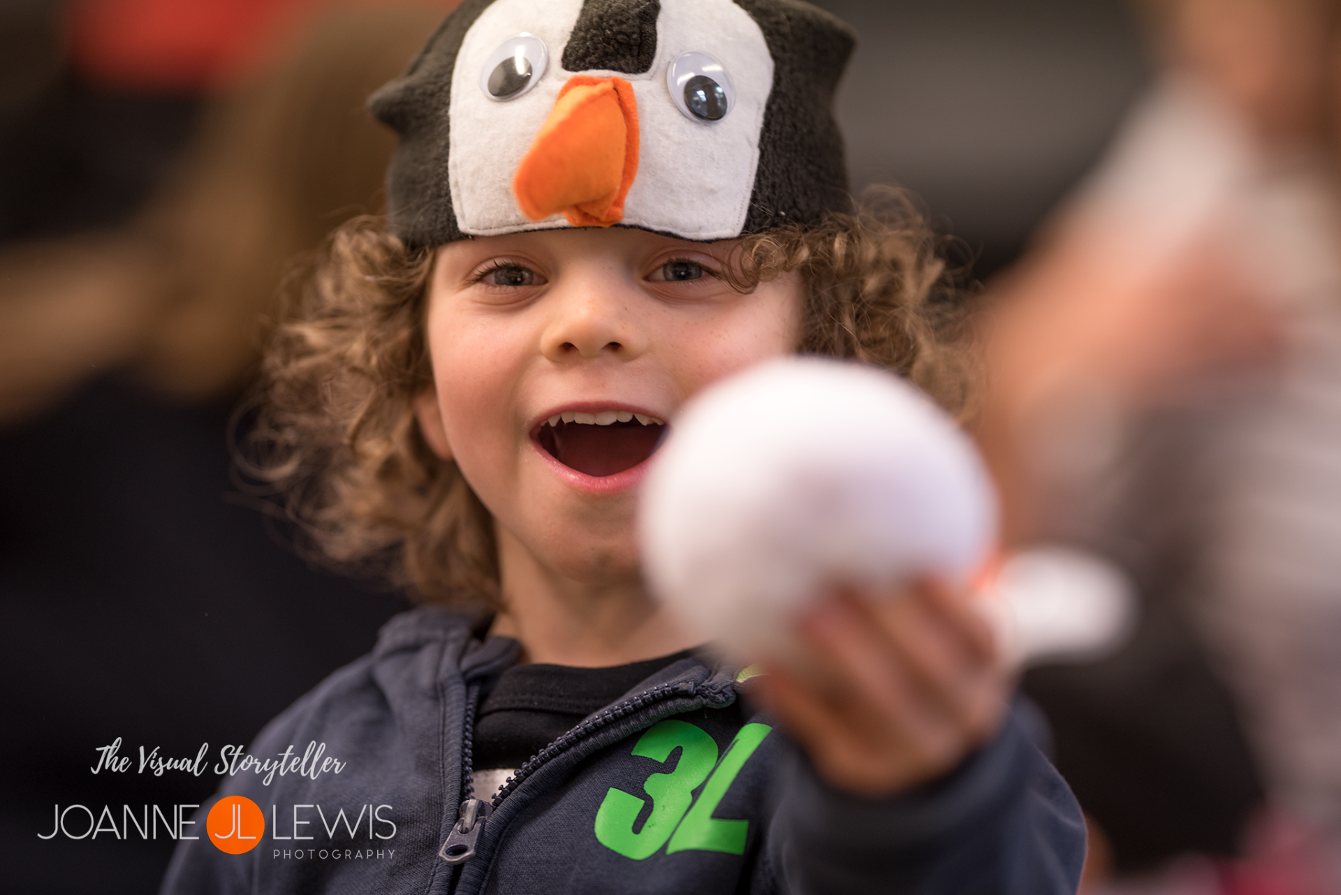 Young boy wearing penguin hat holding a toy snowball