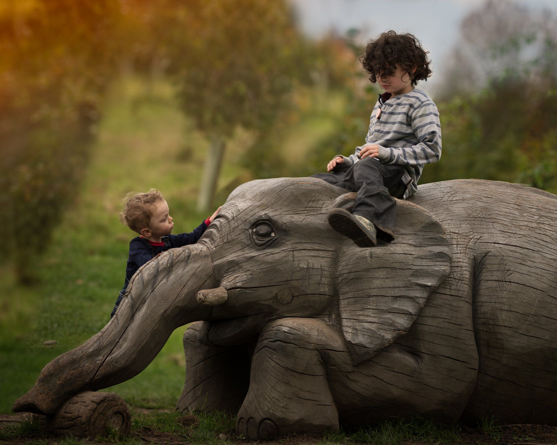 boys playing on a wooden sculpture of an Elephant