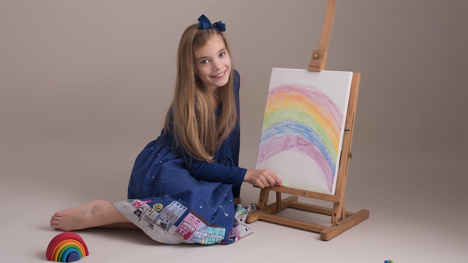 young girl painting a rainbow on canvas in studio photoshoot on neutral background