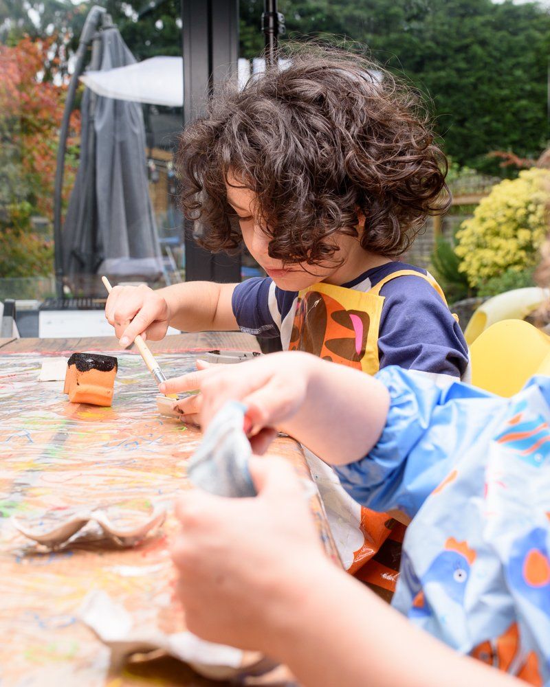 Boy with Dark curly hair painting Halloween egg box bats