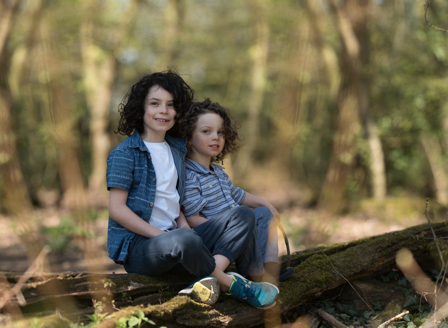 Brothers sitting on a log in the forest in soft sunlight