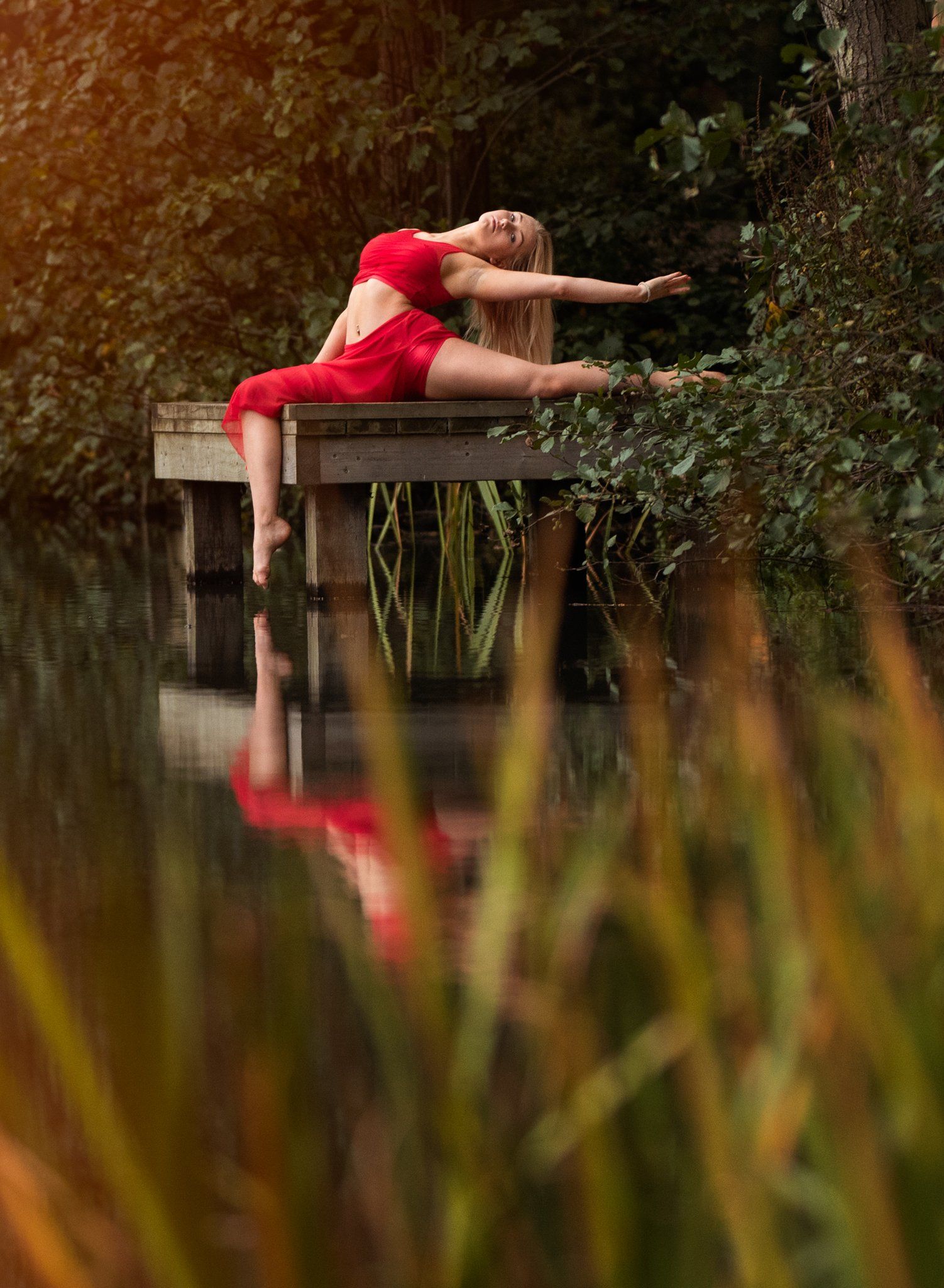 Dancer idipping her toes in the water of a lake sitting on a jetty dressed in red