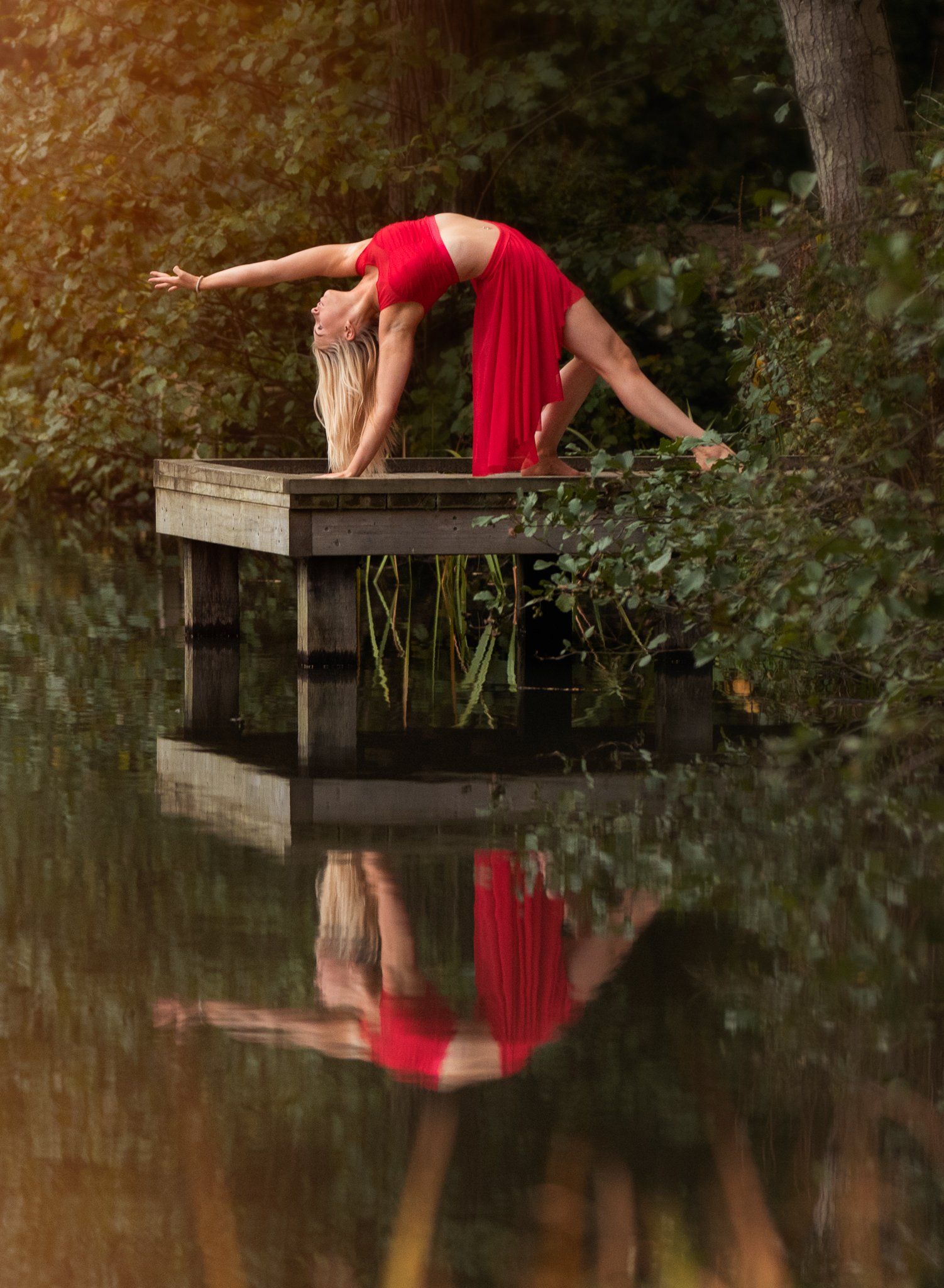 Dancer on a jetty by a beautiful lake wearing a red costume