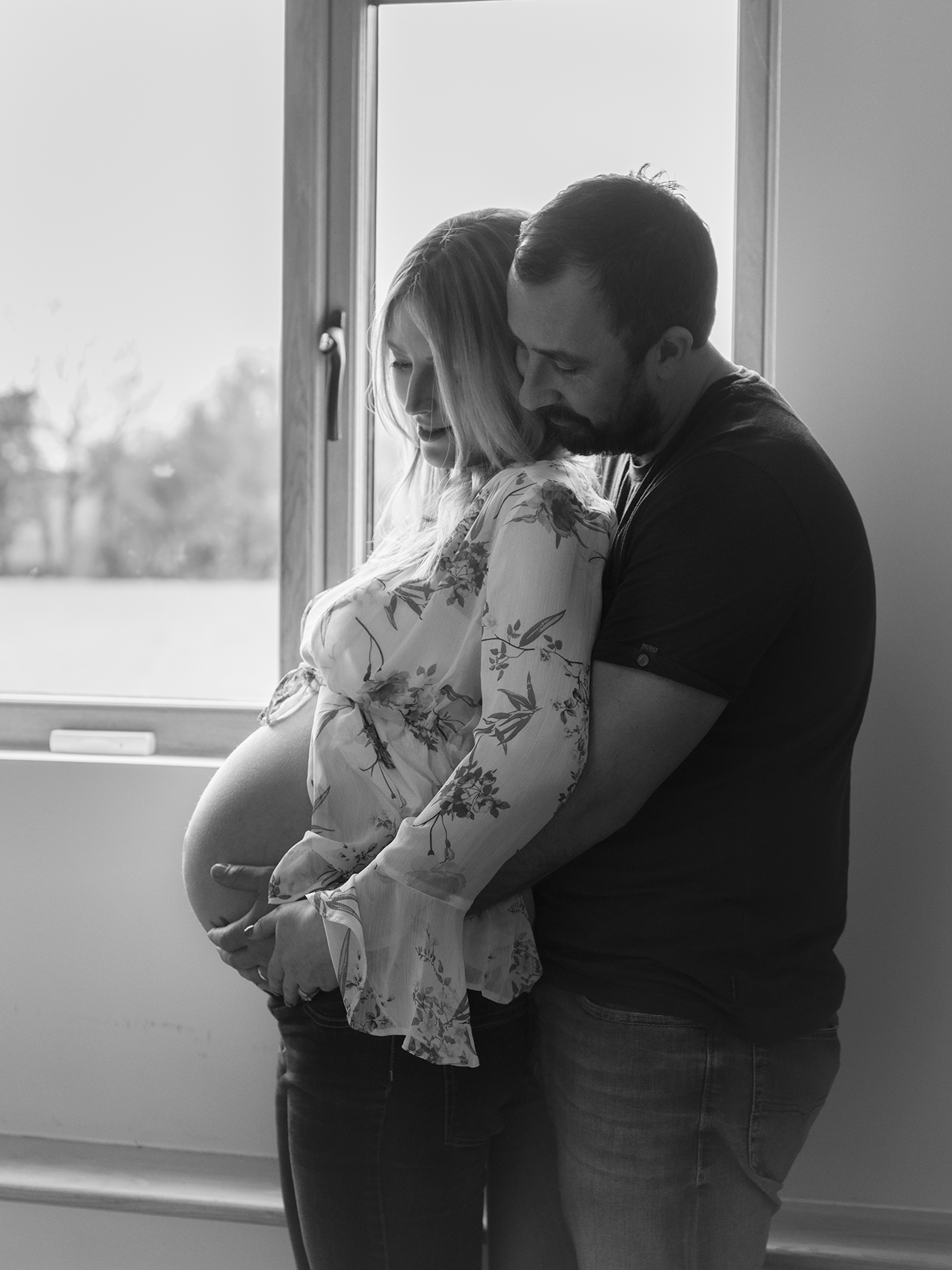 Monochrome backlit couple cuddling pregnant belly for at home natural maternity photoshoot