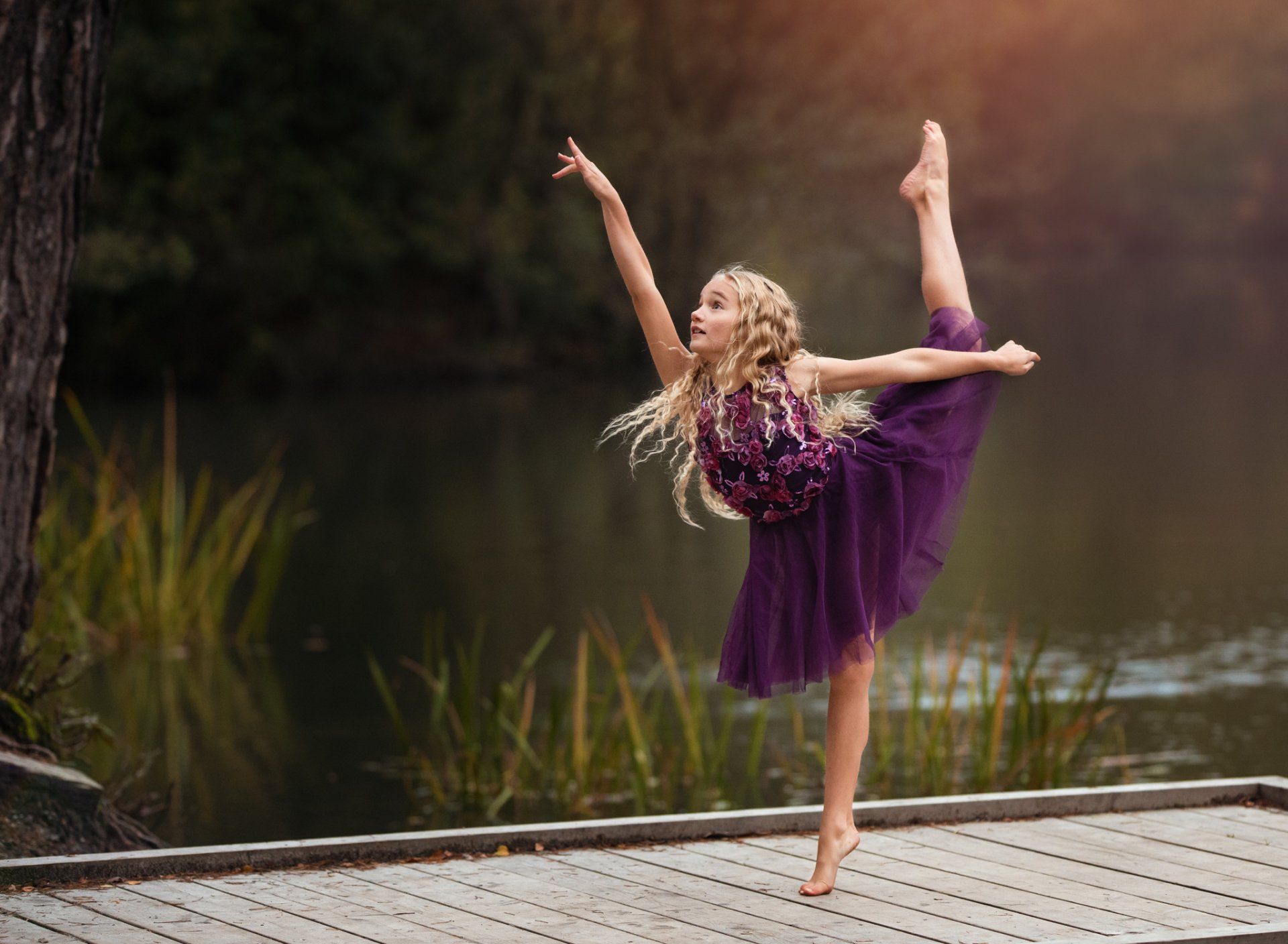 Young female dancer pirouetting at edge of a lake in beautiful purple dress