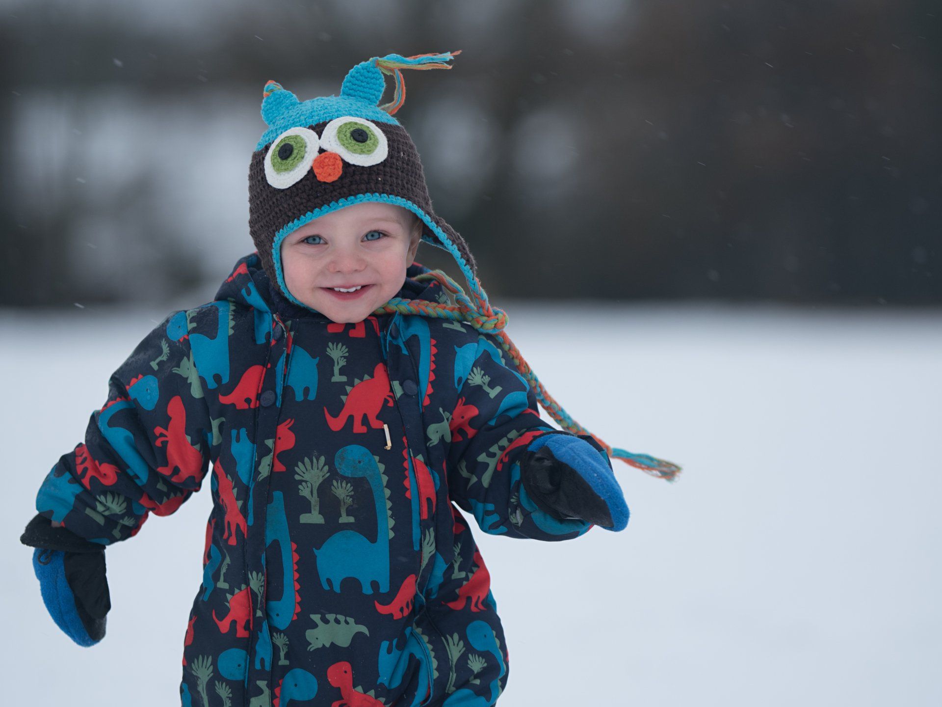 Happy boy walking in the snow wearing snowsuit and Owl hat