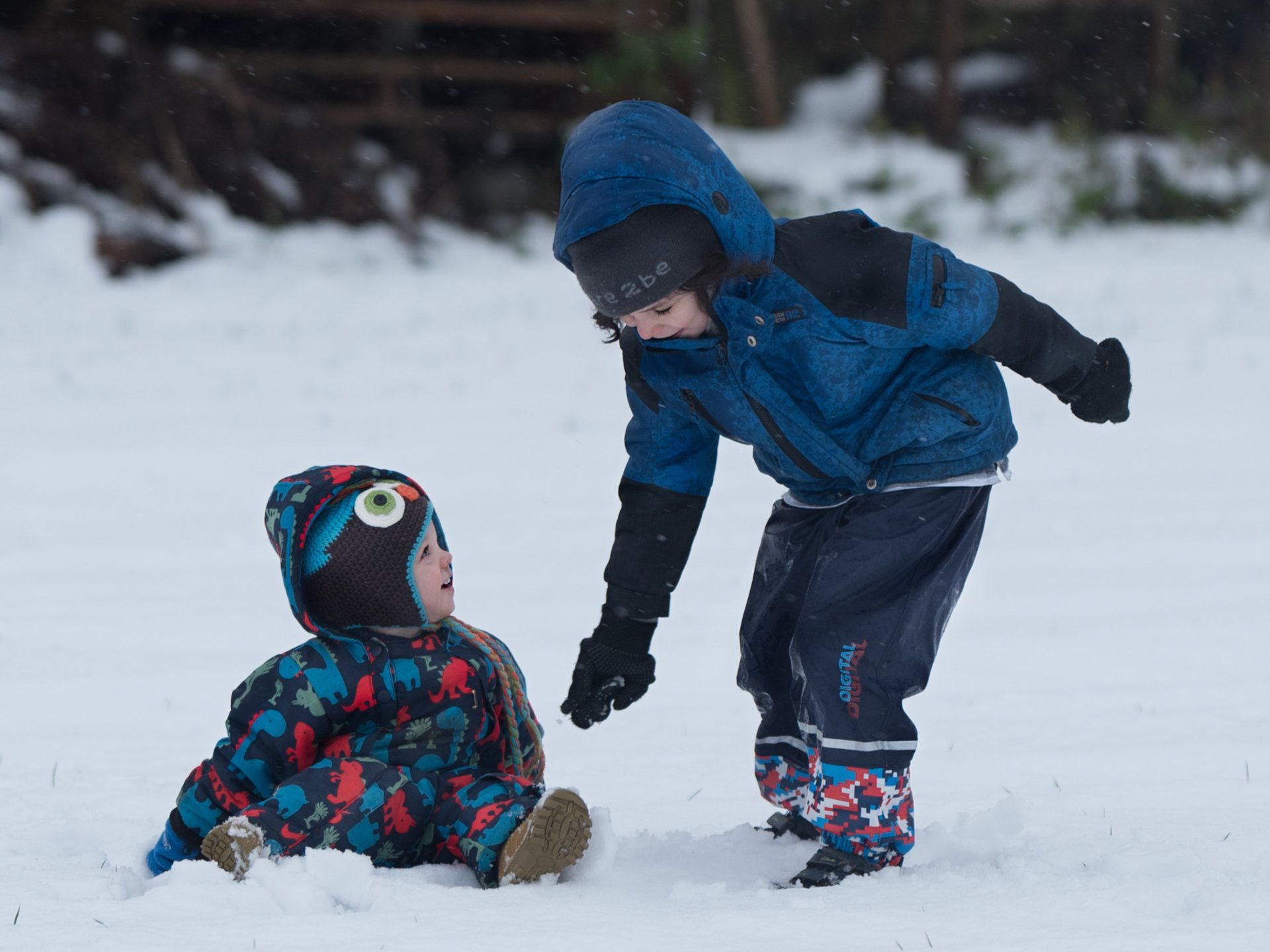 Boy helping his young brother to stand wrapped up in the snow