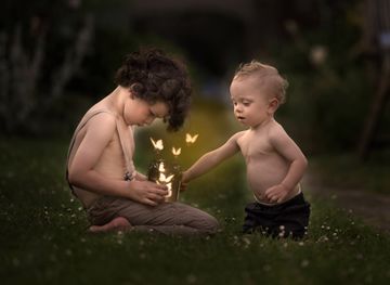 Children sitting in field holding a  magical jar of luminous butterflies