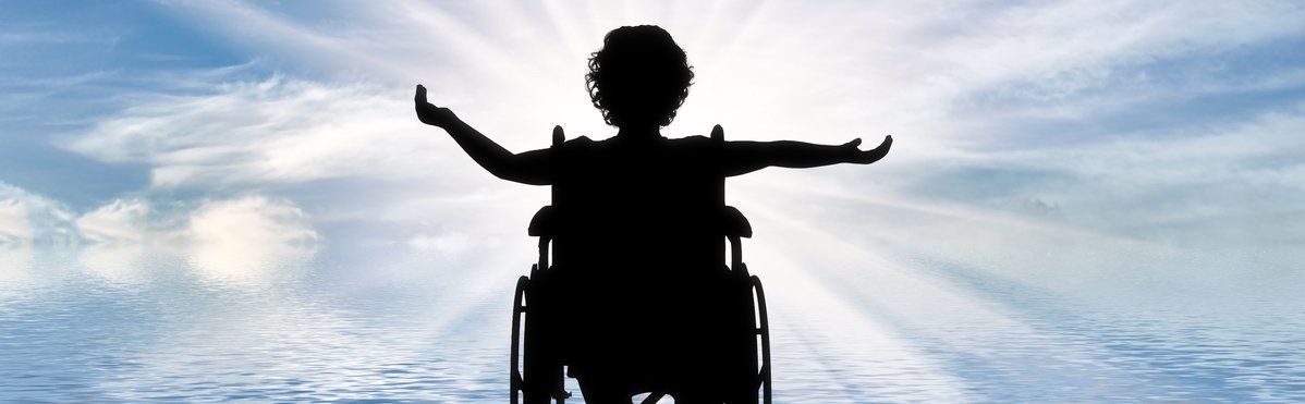 Silhouette of someone in a wheelchair facing a light. Their arms are stretched wide.